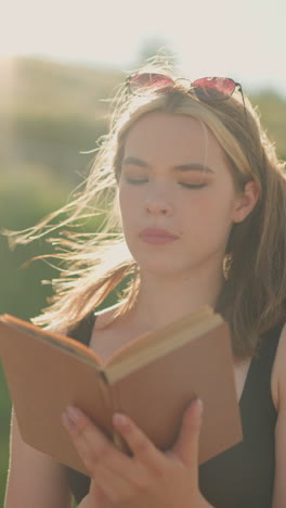 la mujer cierra el libro cubierto de marrón, toma una respiración profunda, y parpadea sus ojos mientras el viento sopla suavemente su cabello, la luz del sol ilumina su cara con un telón de fondo de vegetación y estructuras de madera