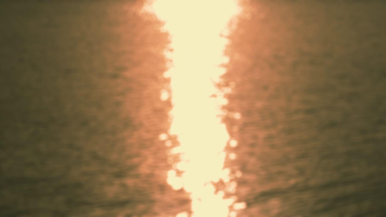 por el mar - bucle sin costuras de una toma de 4k completamente desfocada de una superficie de agua ondulada con un hermoso bokeh de resplandores solares. la escena aparece en vivos colores amarillo, naranja y bronce - prores