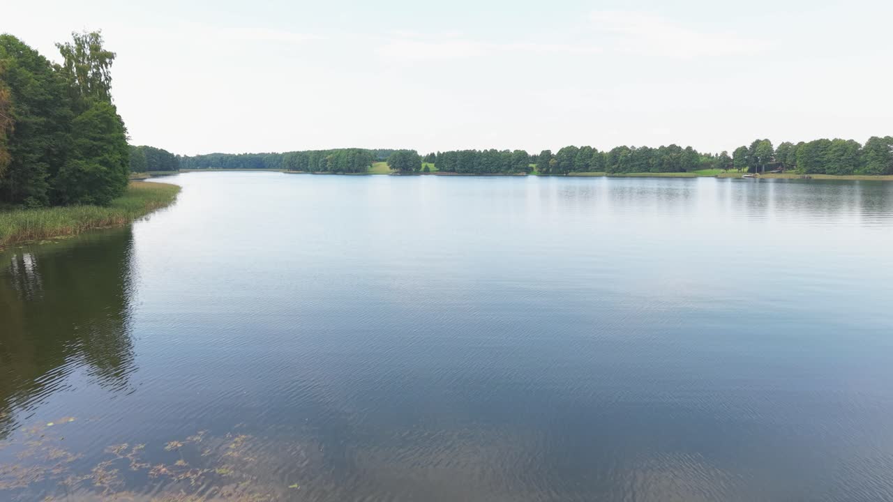 Curved stone path leads through a vibrant green lawn toward a peaceful lakeside surrounded by trees and natural reeds, offering a serene and scenic countryside landscape