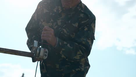 closeup repairman in camouflage cuts metal using disk saw