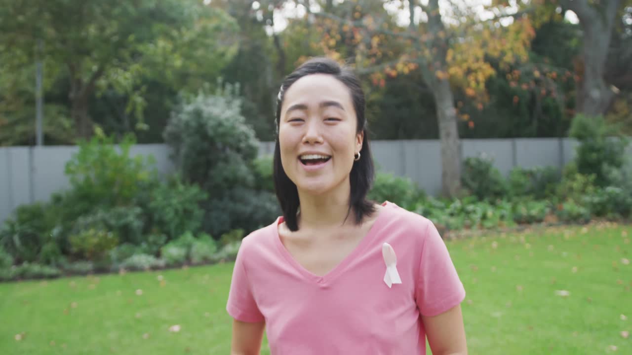 핑크색 티셔츠와 암 리본을 입은 행복한 아시아 여성의 초상화, 정원에서 웃고 서