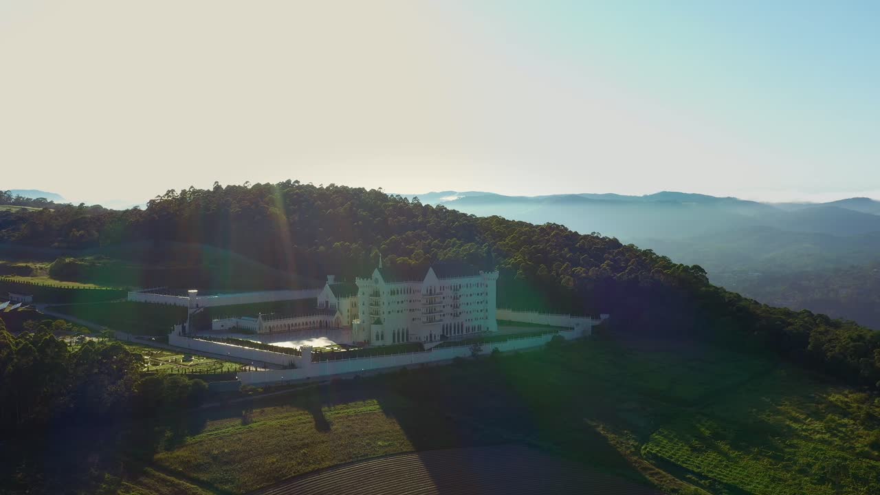 드론이 산 뒤에 태양이 뜨는 수도원 위를 날고 있습니다.