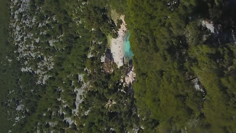 Tilt-down-aerial-reveal-of-Calanque-de-Port-Pin-beach-secluded-in-the-rugged-coastline-of-France---vertical-orientation