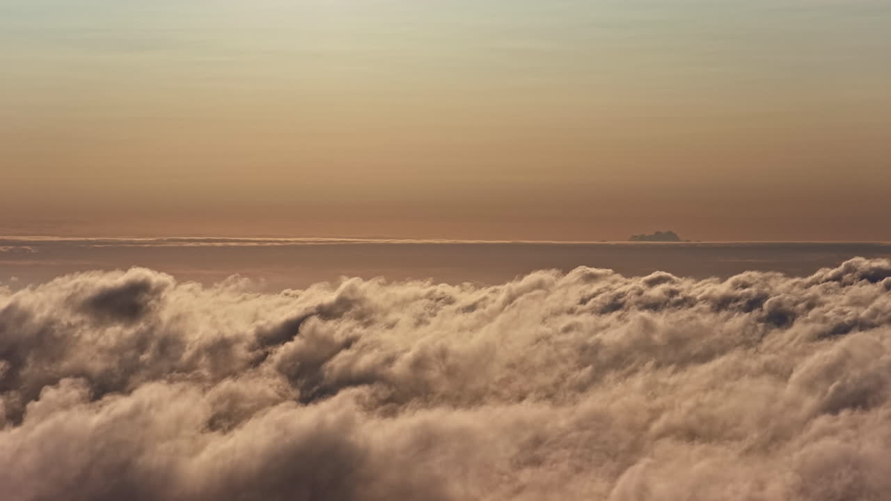 A breathtaking aerial view over a vast sea of clouds at sunset, with a distant, solitary cloud on the horizon creating the illusion of a mysterious mountain peak or island in Latvia