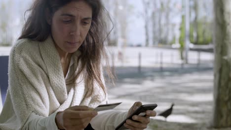 Concentrated-mature-woman-with-credit-card-and-smartphone.