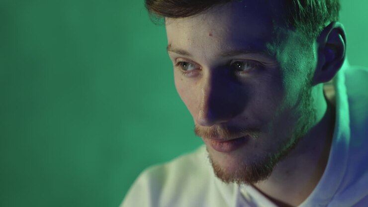 Ritratto di un giovane uomo che usa un computer su uno sfondo colorato con luci al neon. Primo piano.