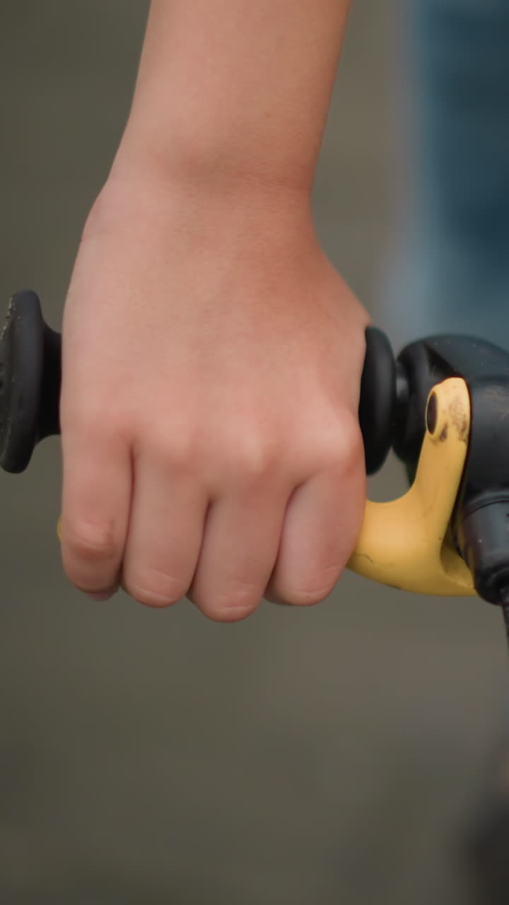 un primer plano de la mano de un niño agarrando el freno de una bicicleta, con una vista borrosa del cuerpo del niño en el fondo