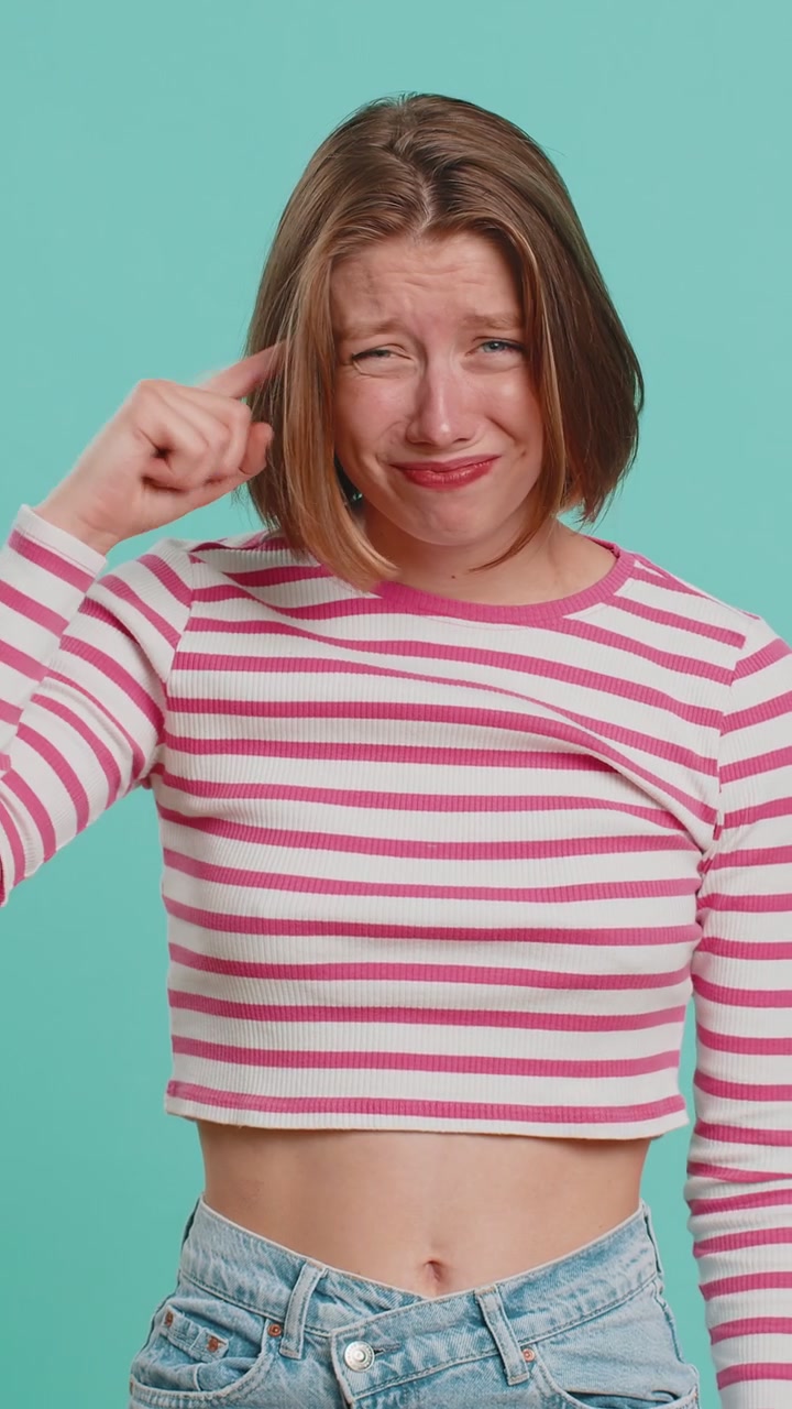 Donna insoddisfatta che indica la telecamera mostra un gesto stupido un dito vicino alla testa idea di piano pazzo stupido