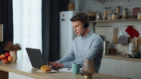 freelancer trabajando escuchando música con auriculares sentado en la mesa de la cocina.