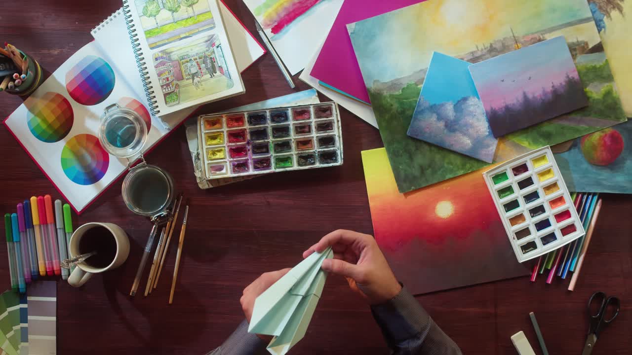 Manos doblando un avión de papel en un escritorio artístico