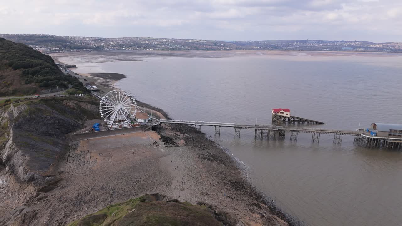 Aerial panoramic establishing orbit of Mumbles Pier in Swansea, UK, with the Big Wheel near the coastline during daytime