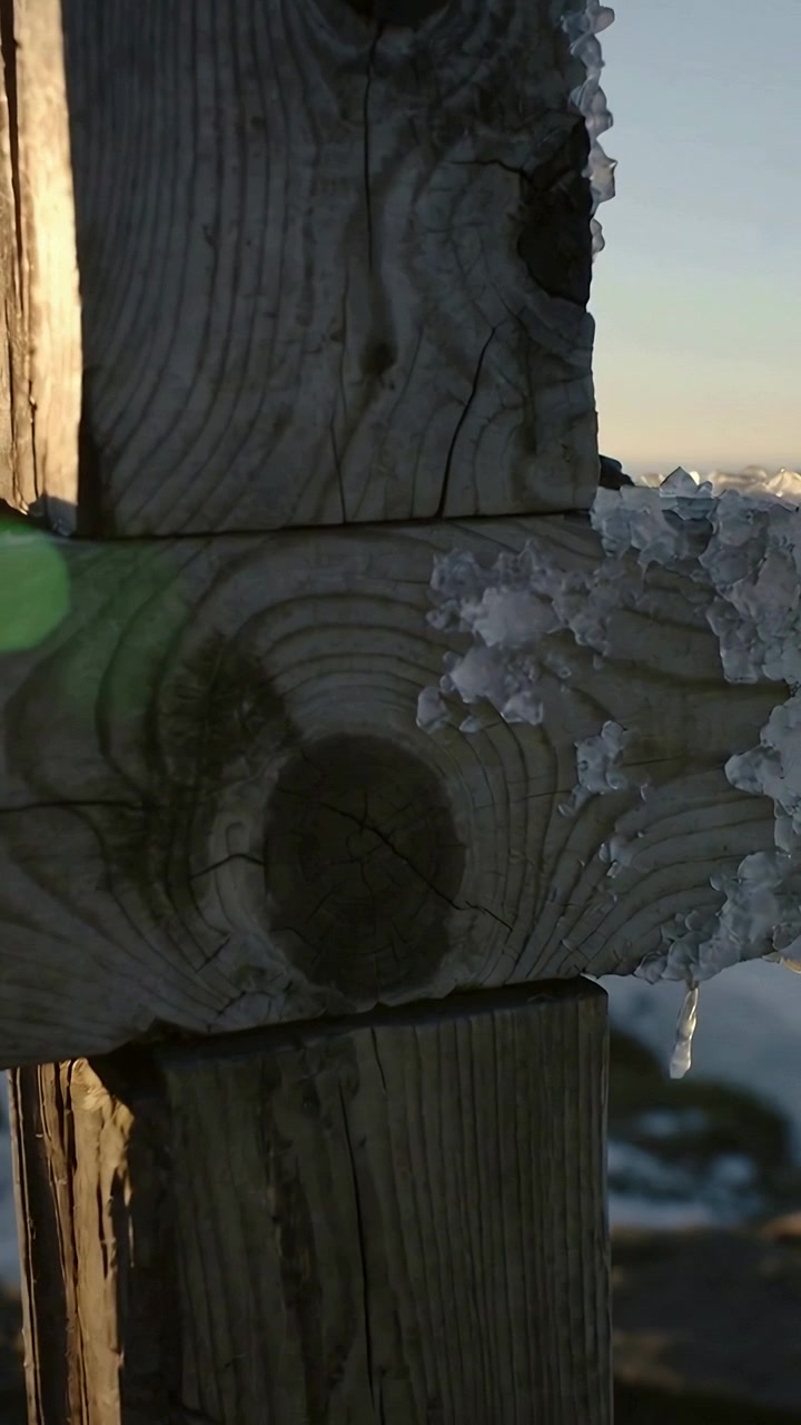 Video verticale: Sole basso, telecamera inclinata che rivela un palo di legno e un ghiacciolo all'alba, ghiaccio scintillante.
