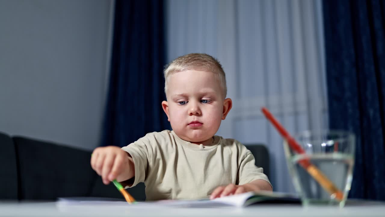 Bambino biondo disegna con i colori. Il bambino piccolo impara a disegnare con i pennelli. Il bambino impara l'arte. Il bambino gioca e impara a disegnare a casa.