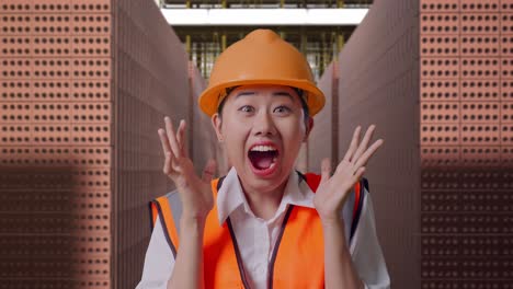 close up of asian female engineer with safety helmet smiling to camera and saying wow while standing with red brick packed in stacks are stored