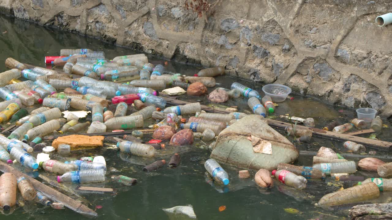 Ampia inquadratura statica di bottiglie di plastica e rifiuti che galleggiano in un fiume inquinato in Thailandia