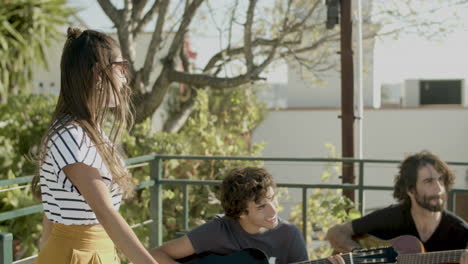 happy girl dancing at rooftop party while men playing guitar