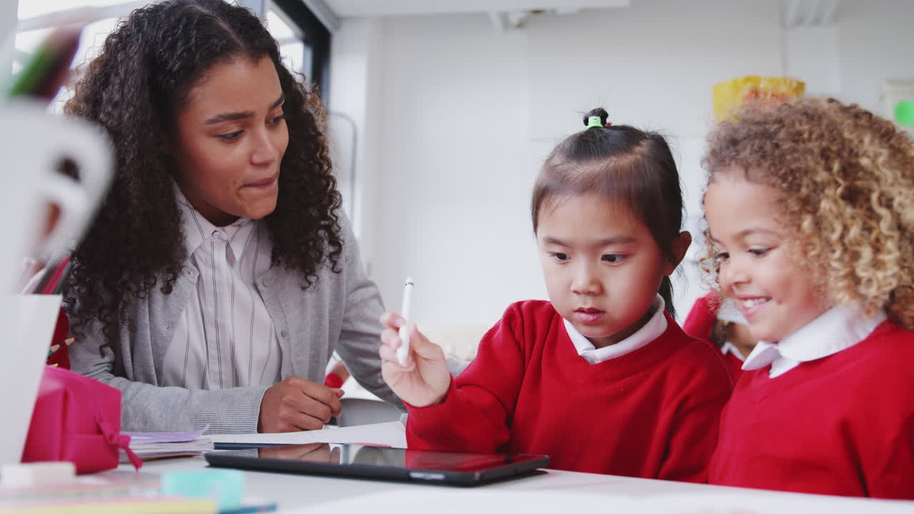 maestra de escuela infantil ayudando a dos escolares usando una tableta y un lápiz, de cerca