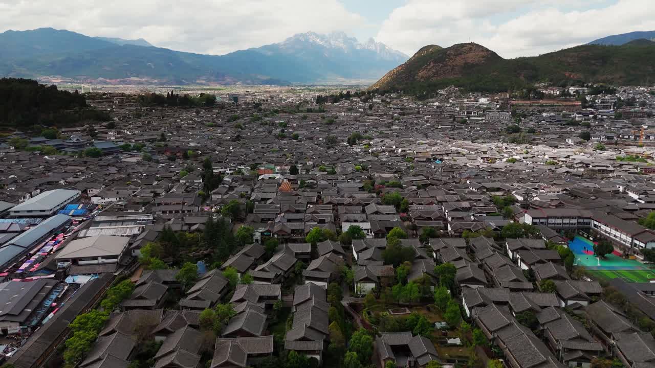 Panoramic aerial descend over Lijiang Old Town revealing surrounding green hills and distant mountains