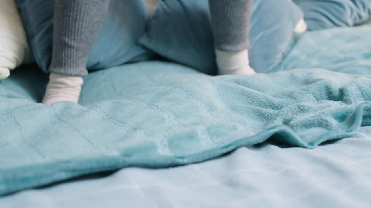 Closeup of child foot in white sock stepping on soft blue blanket on bed, showing playful energy, carefree childhood moment, cozy atmosphere, dynamic indoor movement and joyful home lifestyle