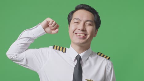 close up of asian man pilot smiling and flexing his bicep while standing in the green screen background studio