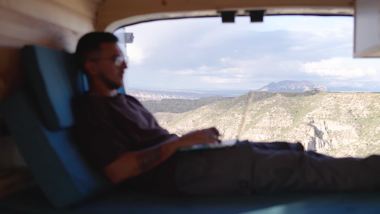 Blurred digital nomad using netbook in campervan with scenic mountain background