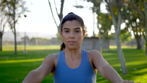 close up on a pretty young hispanic woman working out in the park with dumbbells doing shoulder deltoid raises slow motion