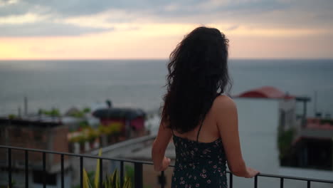 young, brunette woman watching the sunset over the ocean from the rooftop - pull back rack focus