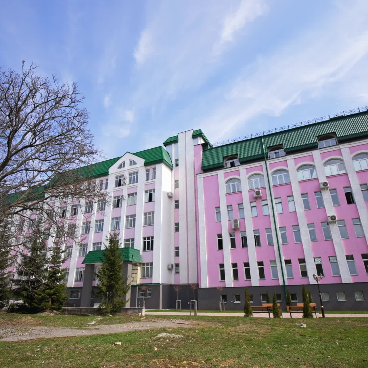 Walking along the big beautiful multi-storey building with green roof. Little park is in front of the building. Low angle view