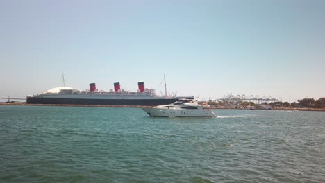 enorme yate privado pasa por la entrada del puerto con un crucero gigante y la reina maría en el fondo