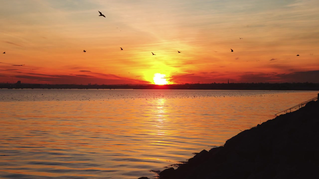 Tyyni auringonlasku Dublinin yllä, liitelevien lintujen ja seesteisten vesien kera.