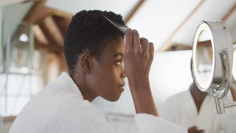 mujer afroamericana atractiva cepillando el cabello en el baño