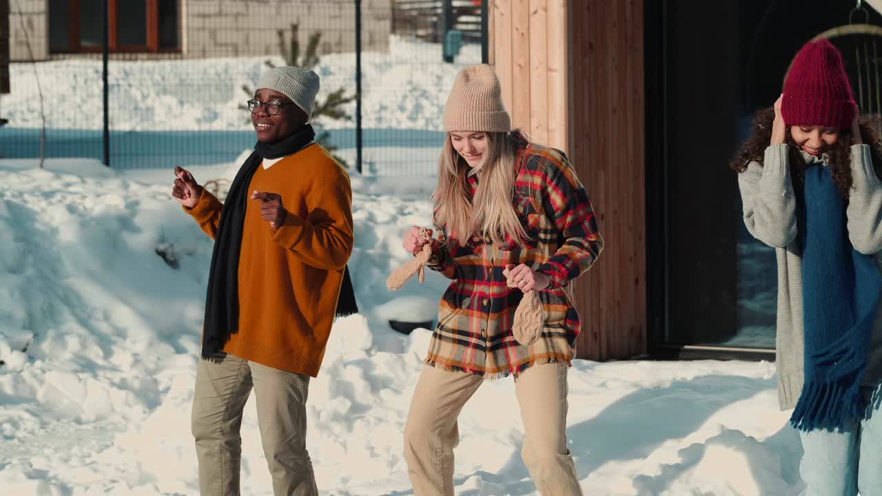 Christmas holiday fun. Group of happy multiethnic young friends dance together at snowy winter house party slow motion.