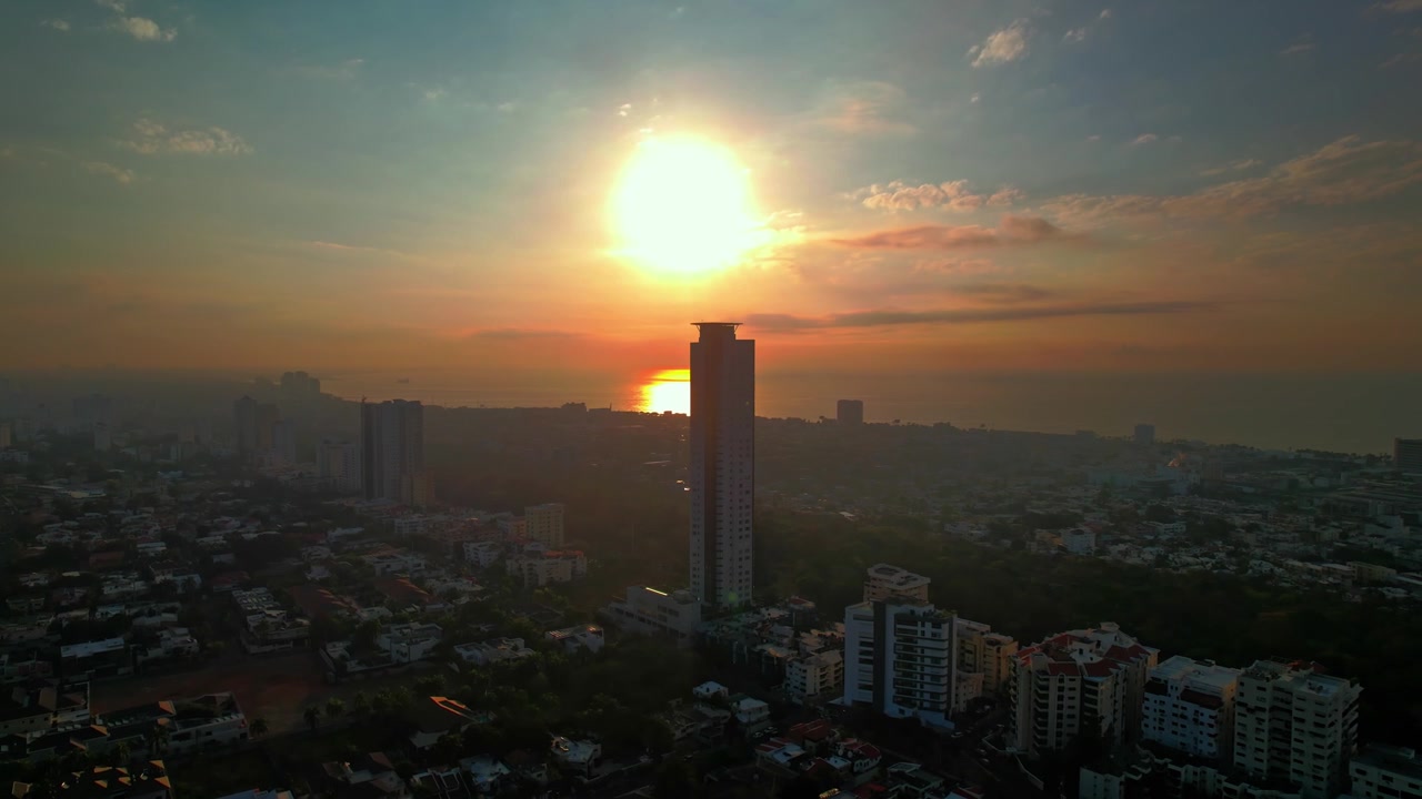 Imagem aérea de drone em ângulo alto avançando e descendo em direção ao icônico arranha-céu Caney Tower, capturando o sol dourado refletindo sobre o mar do Caribe
