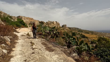 woman walking through arid and rocky terrain on a dry path with cacti and vegetation