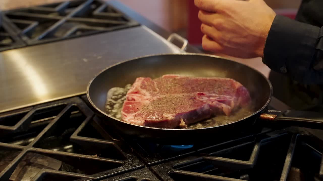 Restaurangkock som kryddar en biff på spishällen