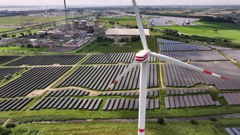 A-wind-turbine-standing-in-a-solar-field,-generating-renewable-energy,-slow-drone-orbit