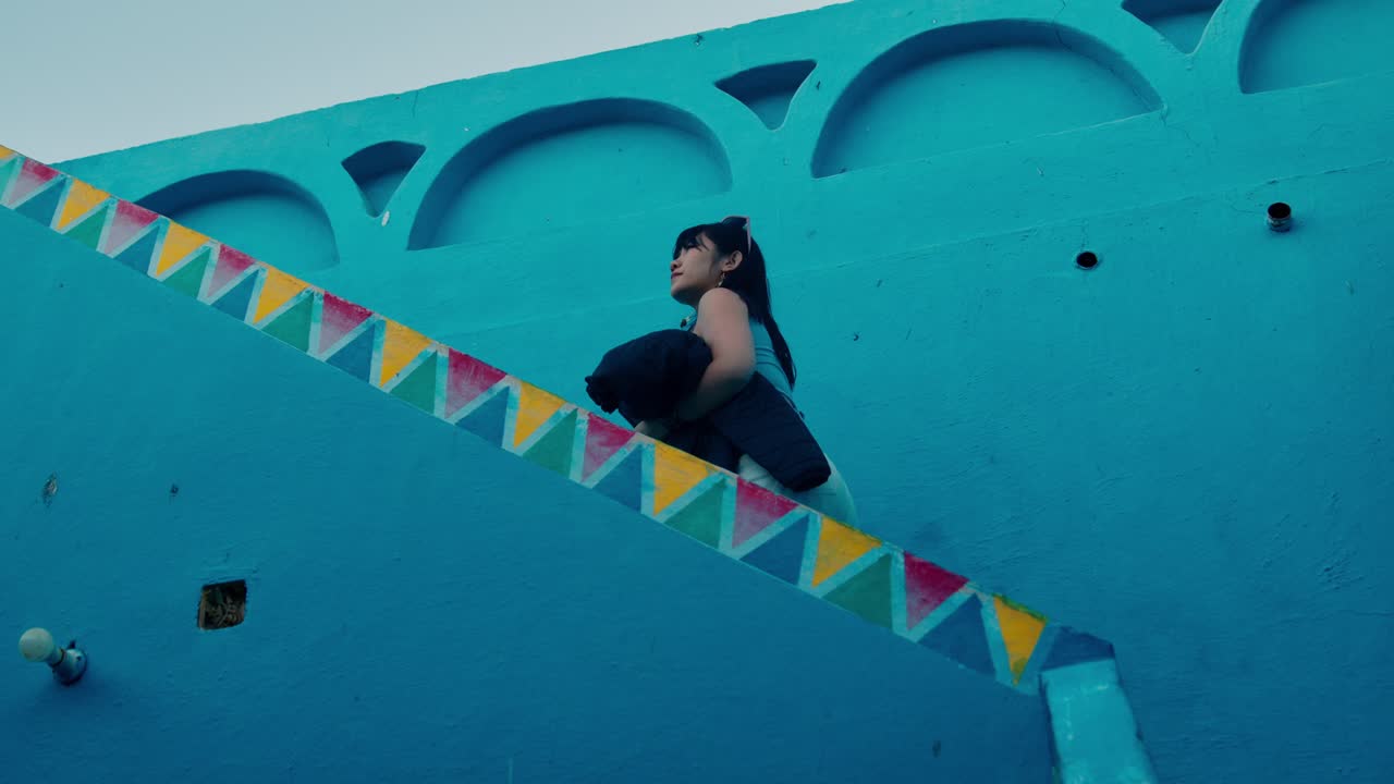 una turista asiática subiendo las escaleras de una colorida casa nubia, aswan, egipto