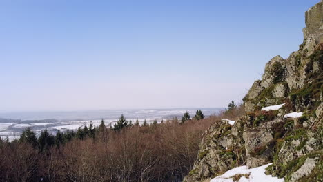 Drone-flight-close-to-a-stony-volcanic-hilltop-in-winter-revealing-a-small-european-town