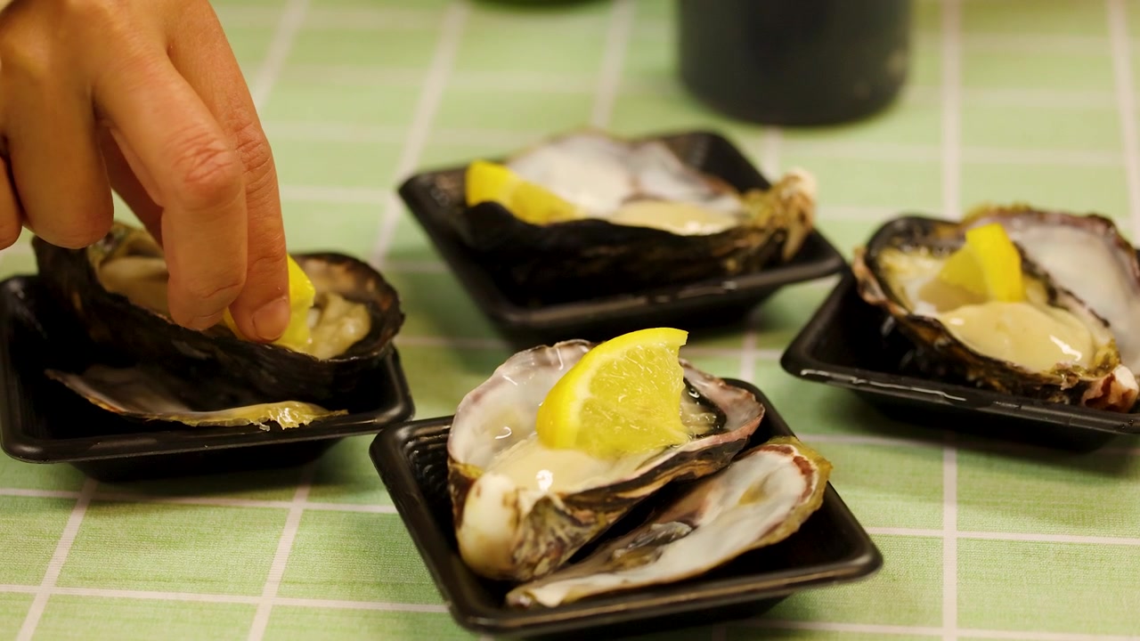 Close-up of a hand squeezing lemon juice onto fresh raw oysters at a Tokyo market.