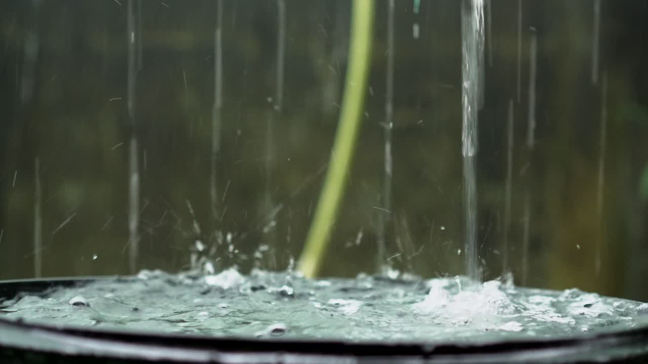 Rain droplets falling and filling up rainwater harvesting barrel, closeup