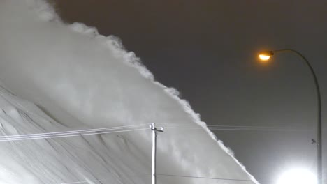 pulverización de nieve desde el soplador de nieve hasta un montón de nieve blanca masiva, limpieza de carreteras por la noche, vista detallada