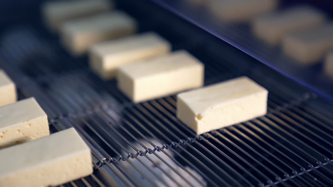 White milky sweets move along the conveyor grid. Producing sweets at the confectionery enterprise. Close up.
