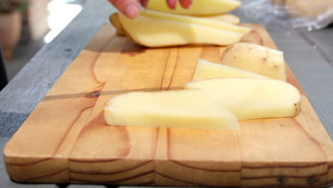 female hands slicing potato into thick cut fries on a wooden chopping board