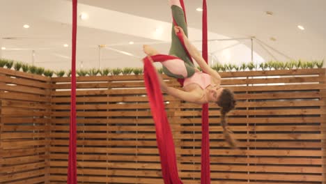 joven morena en un gimnasio mínimo y moderno con divisores de madera haciendo yoga volador con algunas hamacas rojas brillantes, haciendo acrobacias y girando