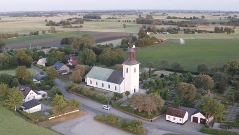 Drone-shot-of-church-with-farming-fields-in-the-background-in-Skane,-Southern-Sweden
