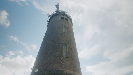 medium wide shot of the lighthouse of sankt peter ording, camera tilts down and pans to the right to reveal more of the scenery, people walking on the dam, blue sky, north sea in the background