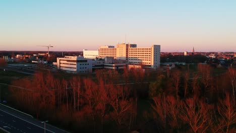 a beautiful drone shot of a hospital surrounded by red trees filmed at sunset