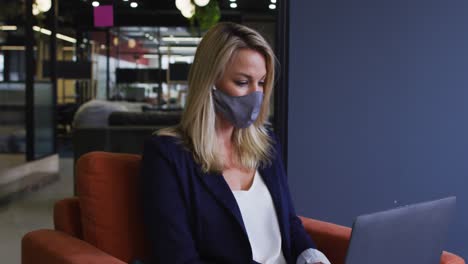 caucasian businesswoman wearing face mask using laptop in modern office