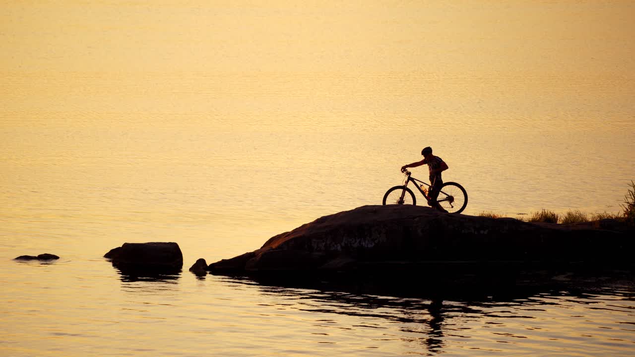 Cyclist in helmet and glasses with his bike near the water. Professional bicyclist comes to the river and washes his hands in water in the evening.