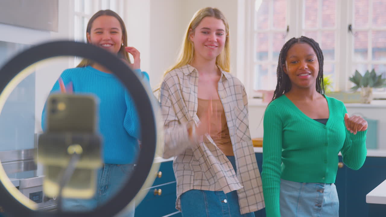 Group Of Teenage Girls In Kitchen Recording Online Dance Video On Mobile Phone For Social Media
